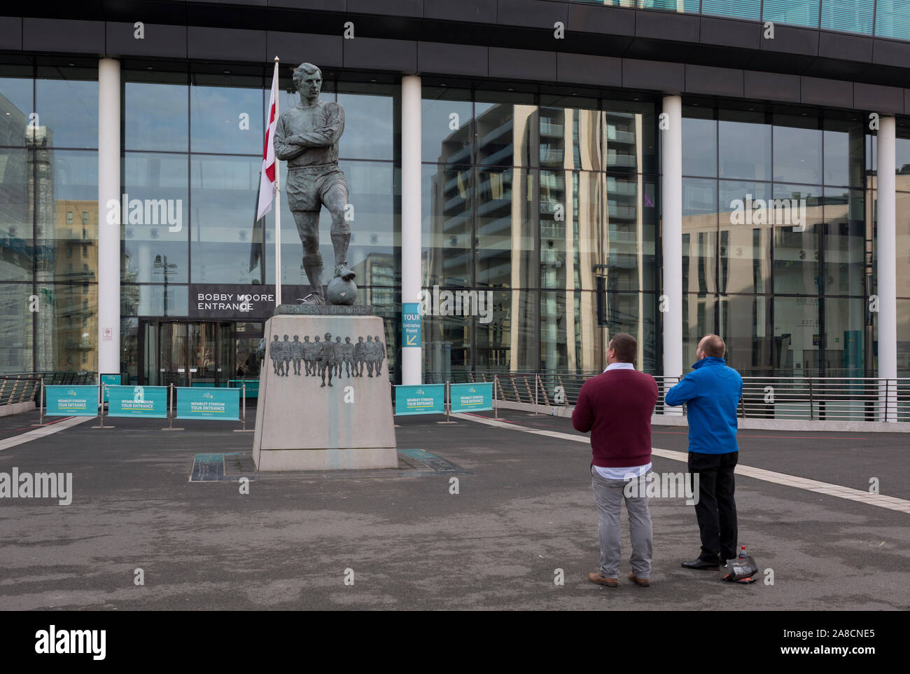 Due i tifosi di calcio di pagare i loro rispetti alla statua del calcio inglese più amato player, Bobby Moore, il 6 novembre 2019, a Wembley, Londra, Inghilterra. Sir Bobby Moore capitanata Inghilterra per la sua vittoria in Coppa del Mondo contro la Germania presso il vecchio stadio di Wembley in 1966. Foto Stock
