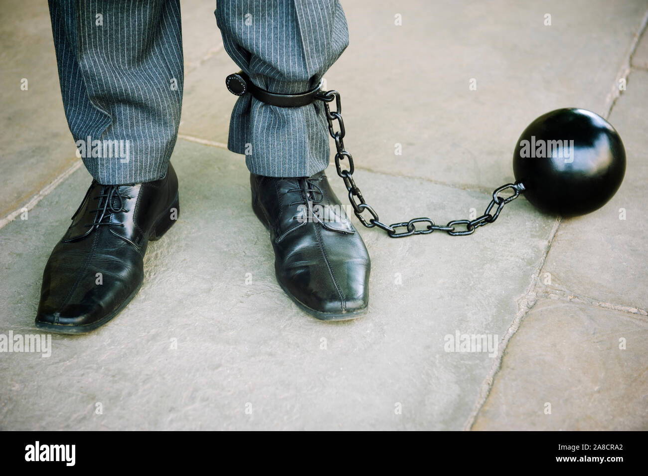Uomo d'affari irriconoscibile in piedi su pavimento in pietra liscia con  grande palla di ferro nero incatenato alla sua caviglia Foto stock - Alamy