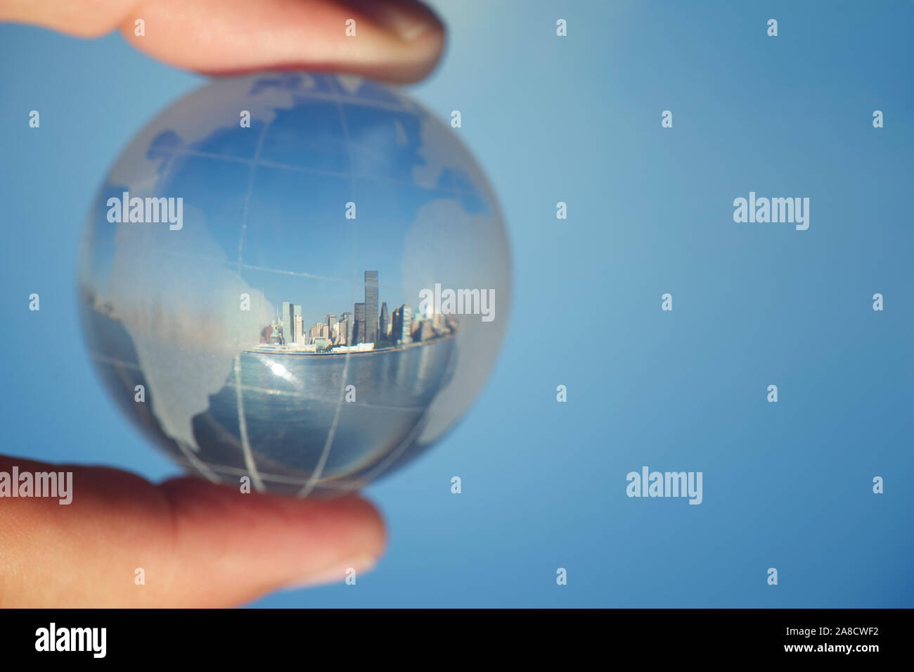 Skyline della città che riflette nella sfera di cristallo globo del mondo tenuto tra le dita contro il cielo blu Foto Stock