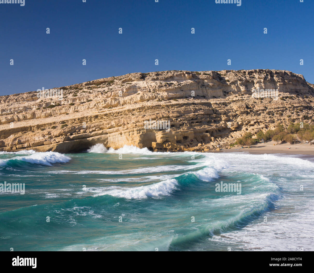 Matala, Heraklion, Creta, Grecia. Onde la battitura della spiaggia sottostante scogliere di arenaria, ex sede della caverna-abitazione hippies. Foto Stock