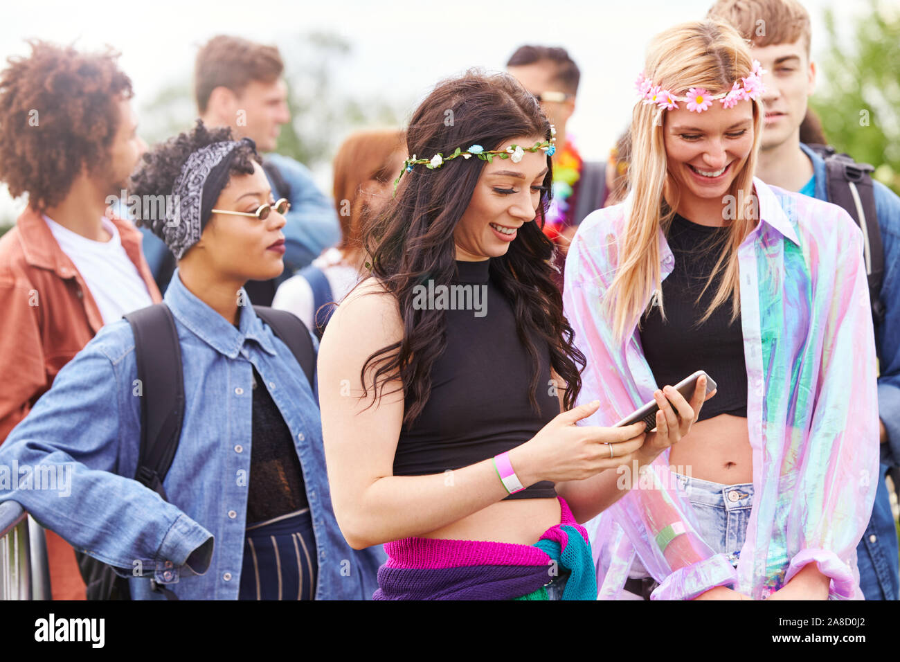 Amici di sesso femminile guardare al telefono mobile come essi attendere  dietro la barriera in ingresso al Festival di musica sito Foto stock - Alamy