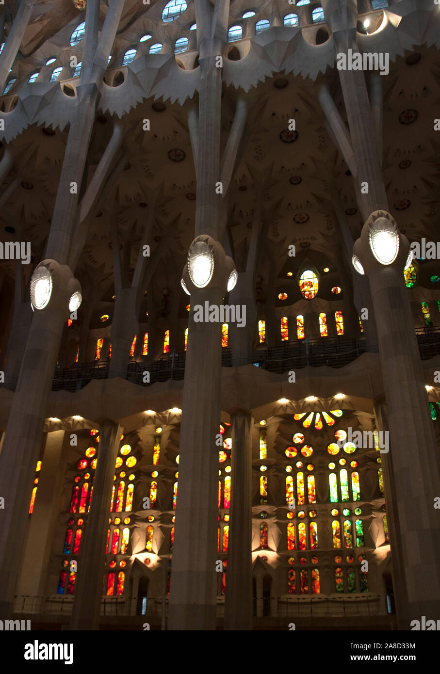 La Sagrada Familia - interno. Righe di grandi finestre di vetro macchiate in colori caldi e alte colonne. Foto Stock