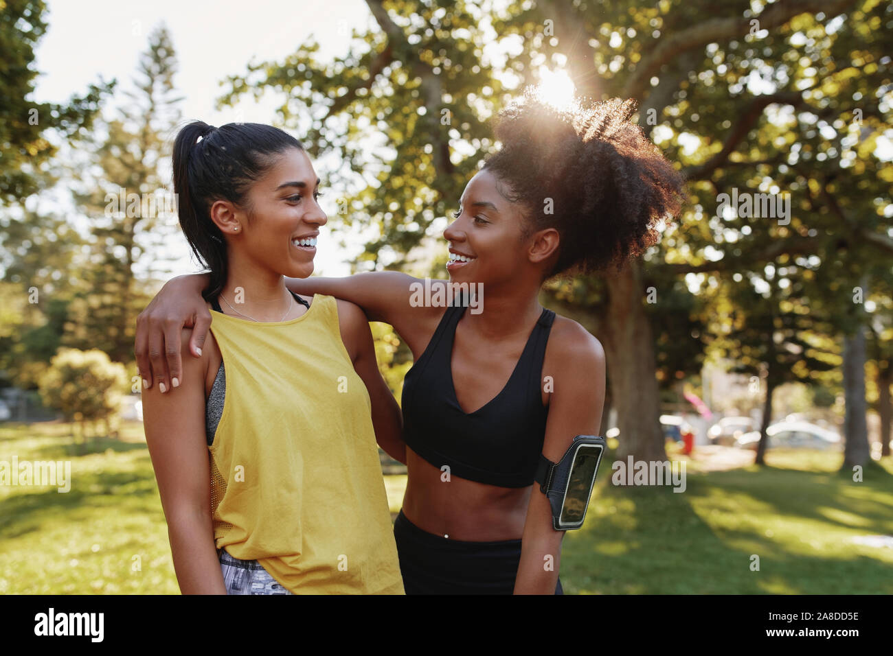 Ritratto di un sorridente multietnica femmina abbracci di amici in un parco sulla giornata d'estate - happy esercizio amici sorridere insieme in un parco Foto Stock