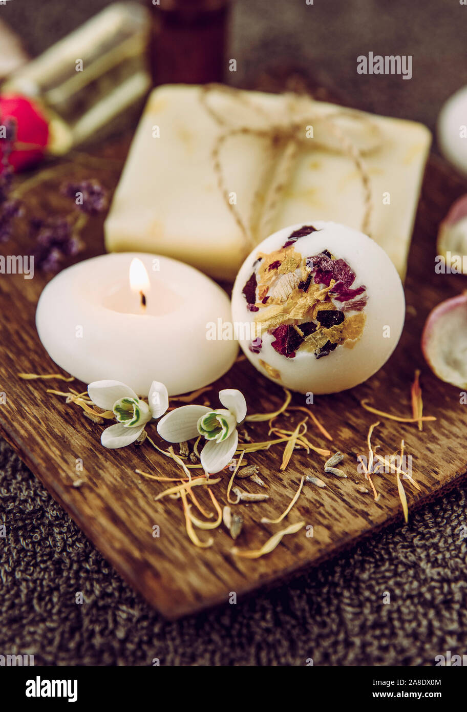 Varie bagno spa prodotti in legno marrone vassoio bagno cremoso bomba, sapone naturale bar con cotone stringa, essiccato di petali di fiori, spa candele accese, essenziale Foto Stock