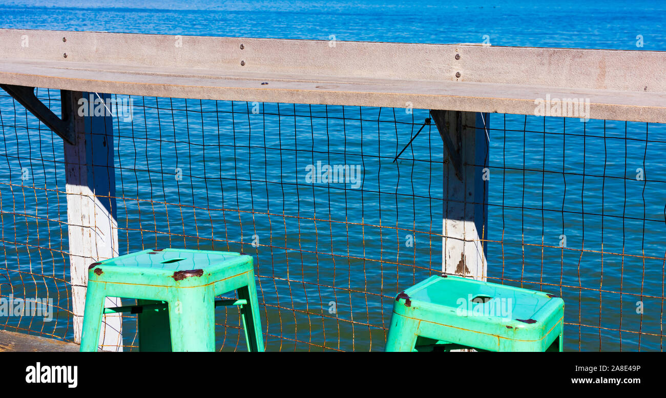 Verde Sgabello in metallo con foro per la maniglia. Il molo di legno della ringhiera sul lungomare di blu. Concetto o simbolo - vacanze, viaggi e relax Foto Stock