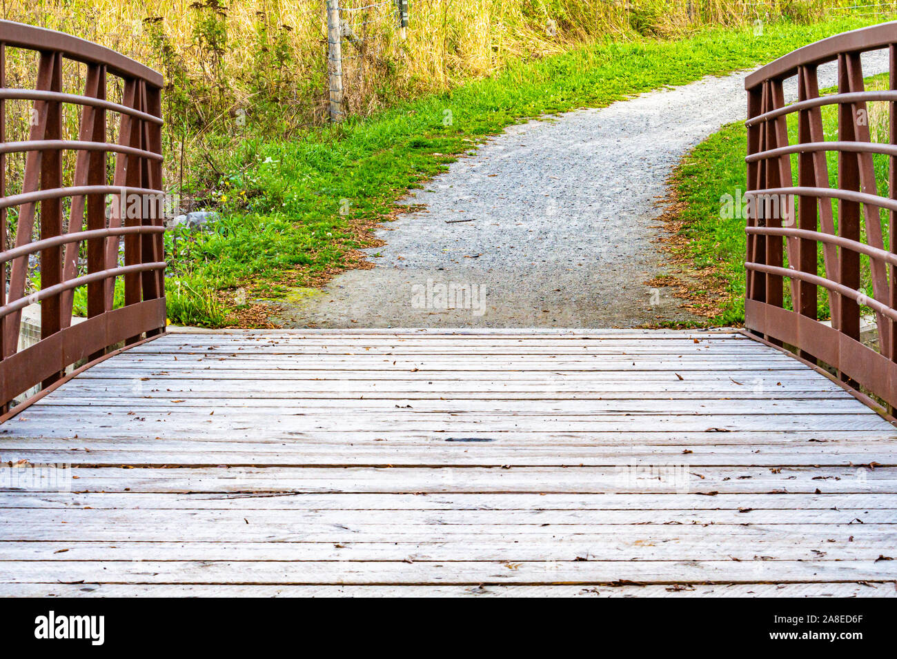 Una passerella con una passerella in legno e metallo arrugginito ringhiere è visto dal suo centro come archi verso il basso e verso un sentiero di ghiaia. Il percorso si trasforma in quanto Foto Stock