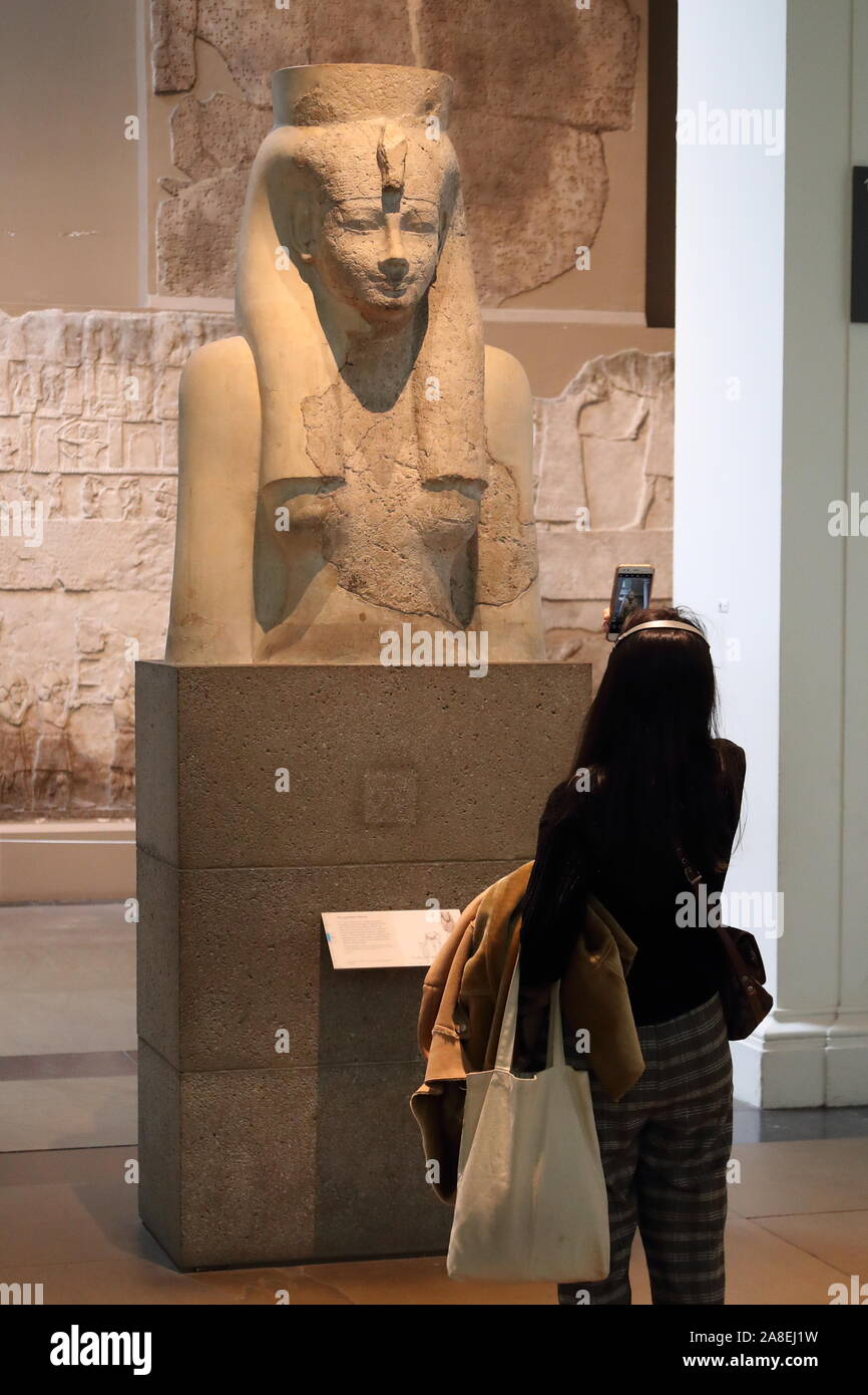 Una donna sta studiando un busto raffigurante la dea egiziana Hathor presso il British Museum di Londra, Regno Unito Foto Stock