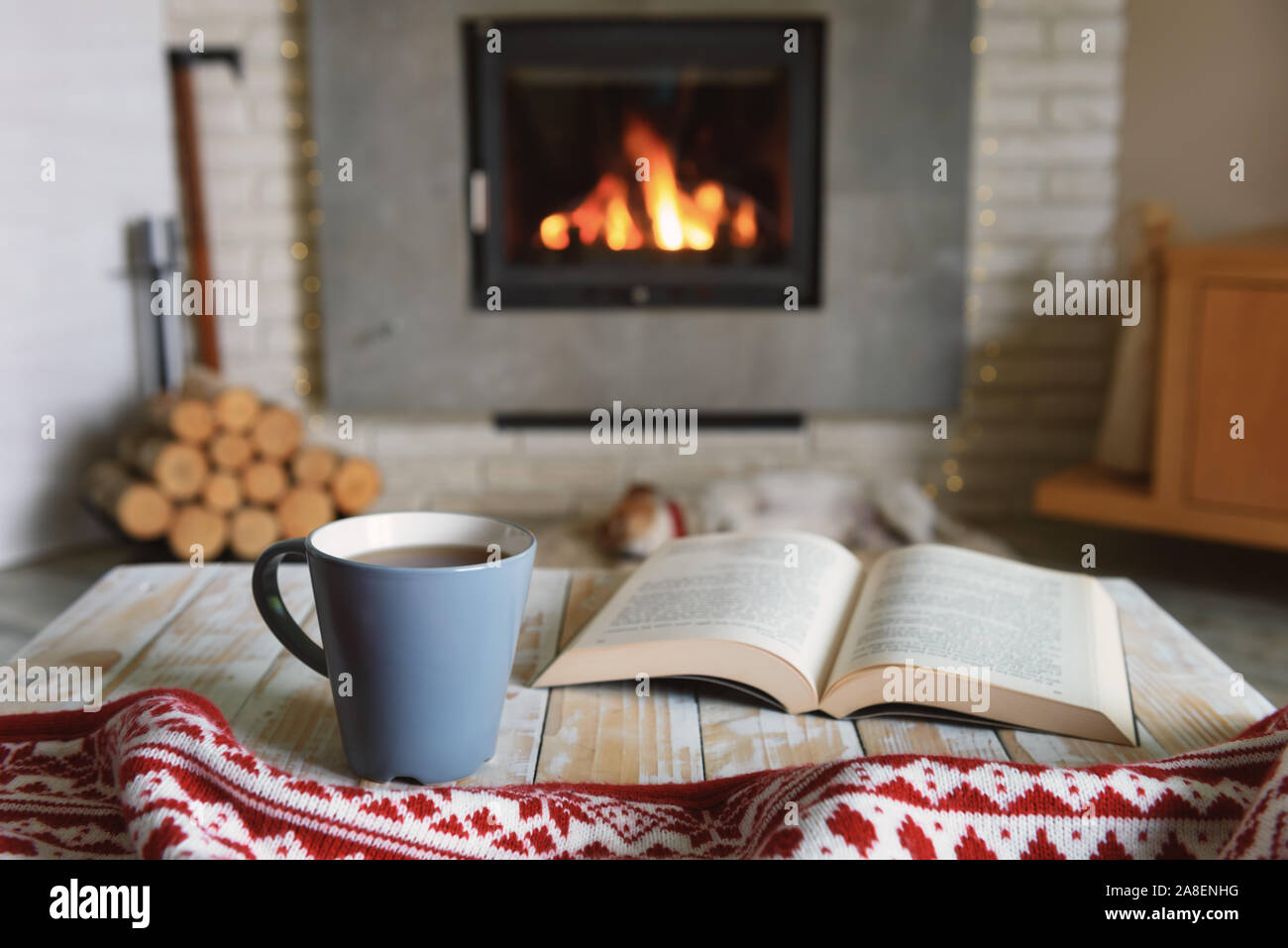 Concetto di Hygge con libro aperto e la tazza di tè vicino al caminetto Foto Stock