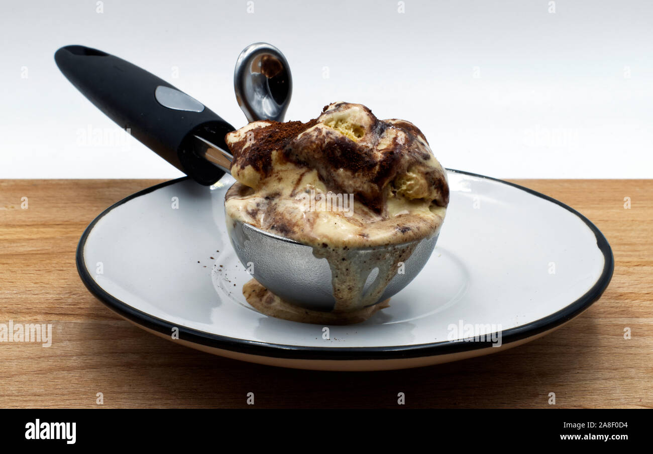 Il tiramisù gelato e un gelato cucchiaio sul tavolo di legno, sfondo bianco. Foto Stock