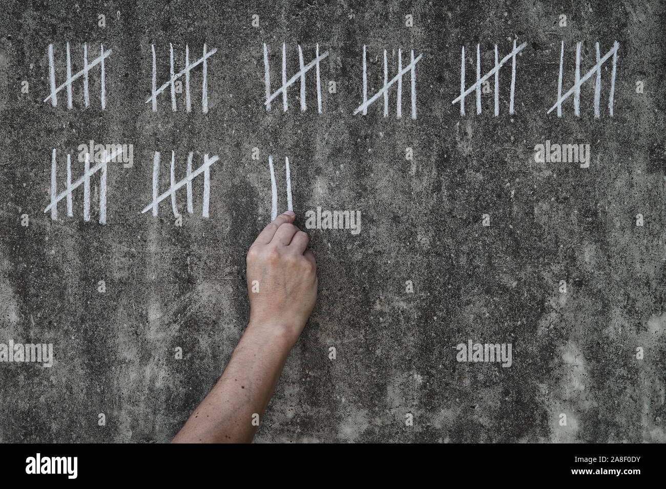 Conteggio dei giorni in prigione - prigioniero maschio scrivere righe bianche di gesso su una sporca parete in calcestruzzo Foto Stock
