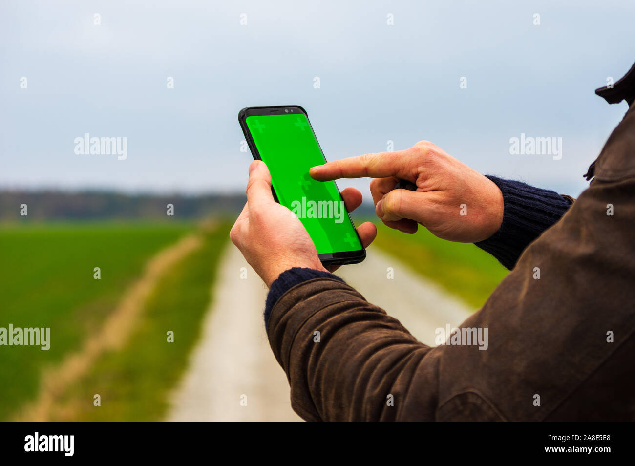 Escursionismo uomo con giacca di pelle usando il suo smart phone per navigare in aperto paesaggio autunnale. Utilizzando un telefono cellulare per controllare la mappa all'aperto Foto Stock