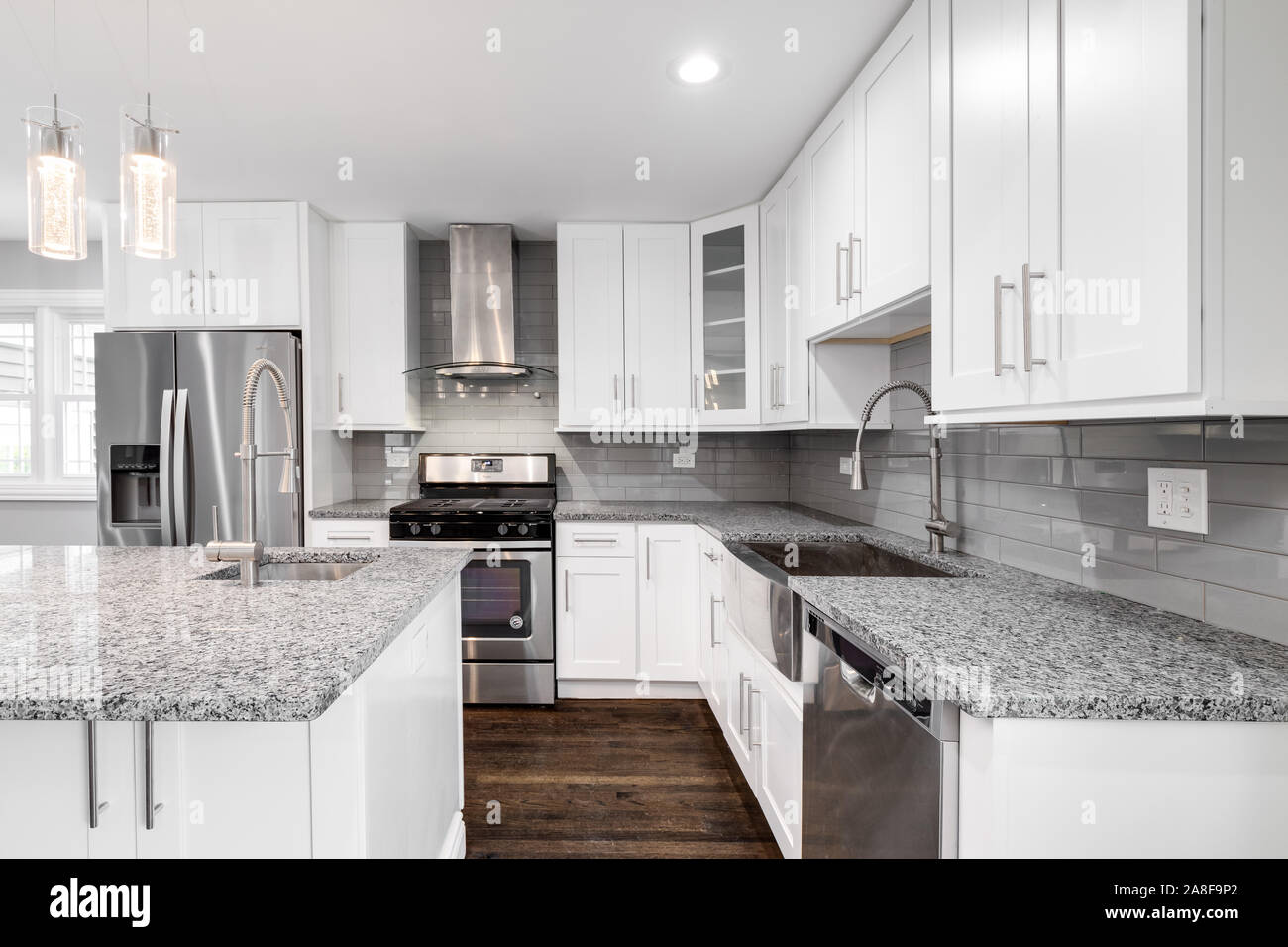 Un elegante e moderna cucina dotata di grigio e bianco screziato di granito, elettrodomestici di acciaio inossidabile, con armadi bianco ed elettrodomestici di acciaio inossidabile. Foto Stock