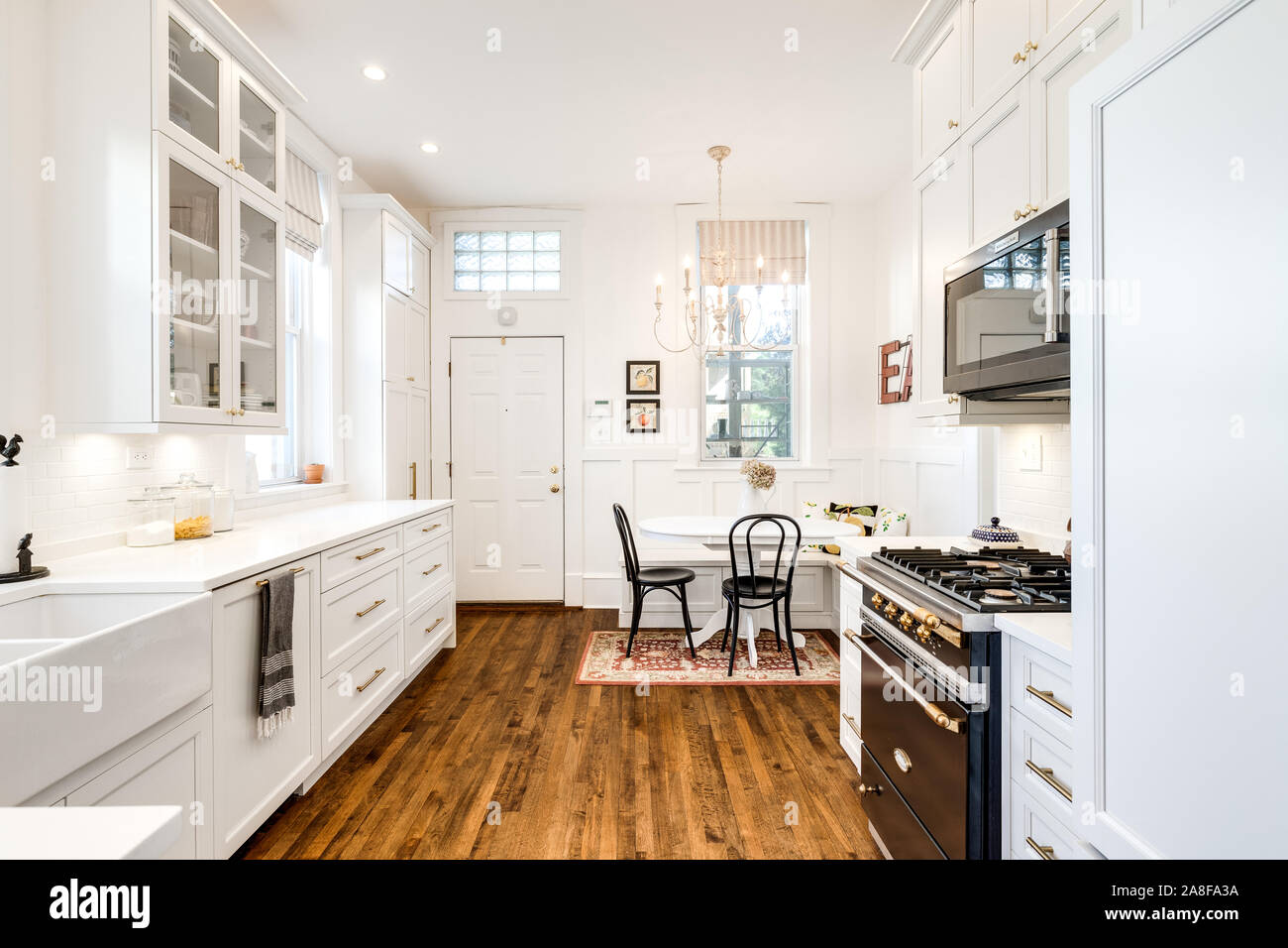 Una cucina bianca con una piccola sala da pranzo in un angolo e pavimenti in legno ovunque. Foto Stock