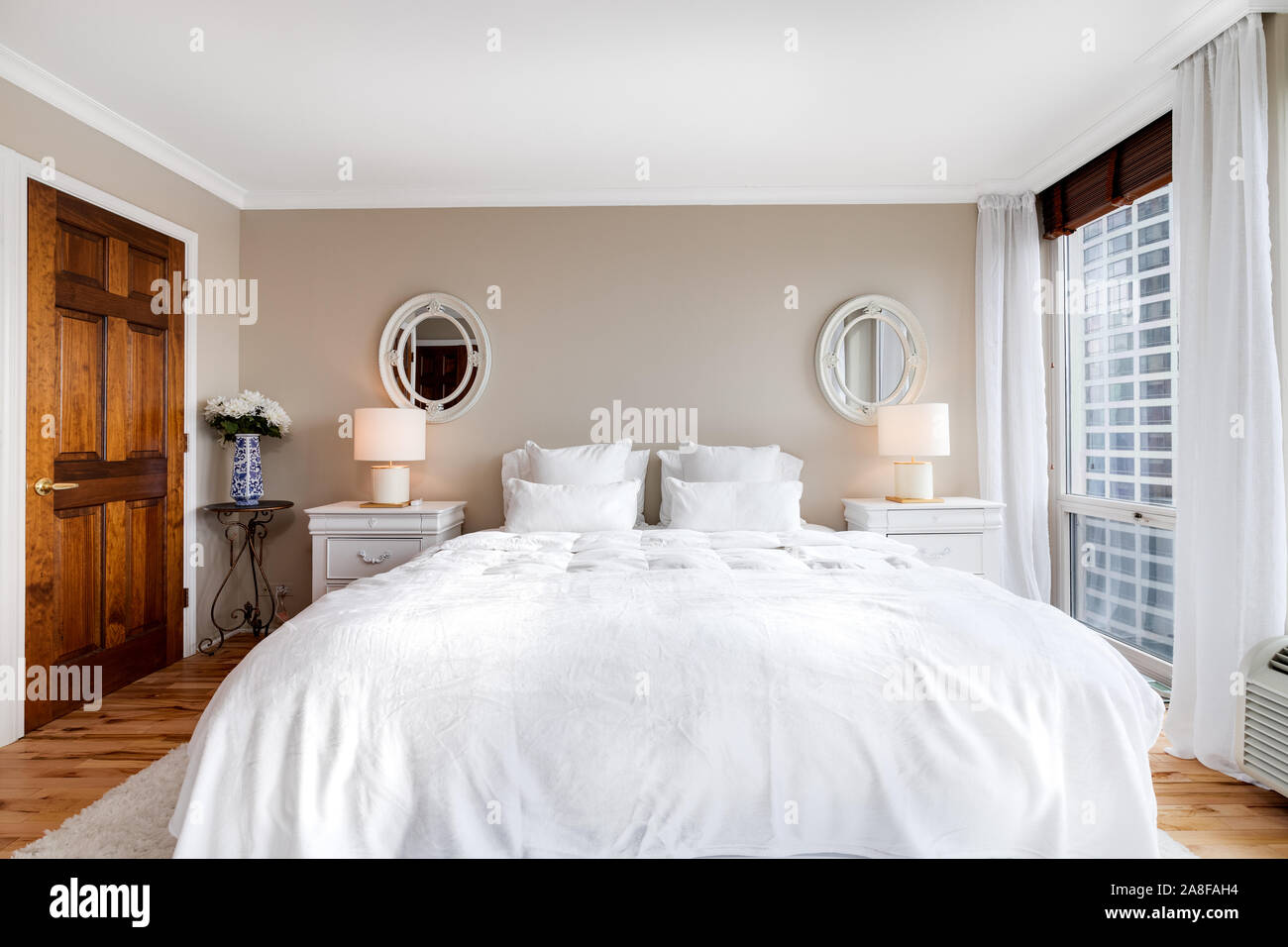 Una grande camera da letto principale si trova nel centro cittadino di Chicago con un letto king size con lenzuola bianche, pareti beige e grande armadio in legno Porte. Foto Stock