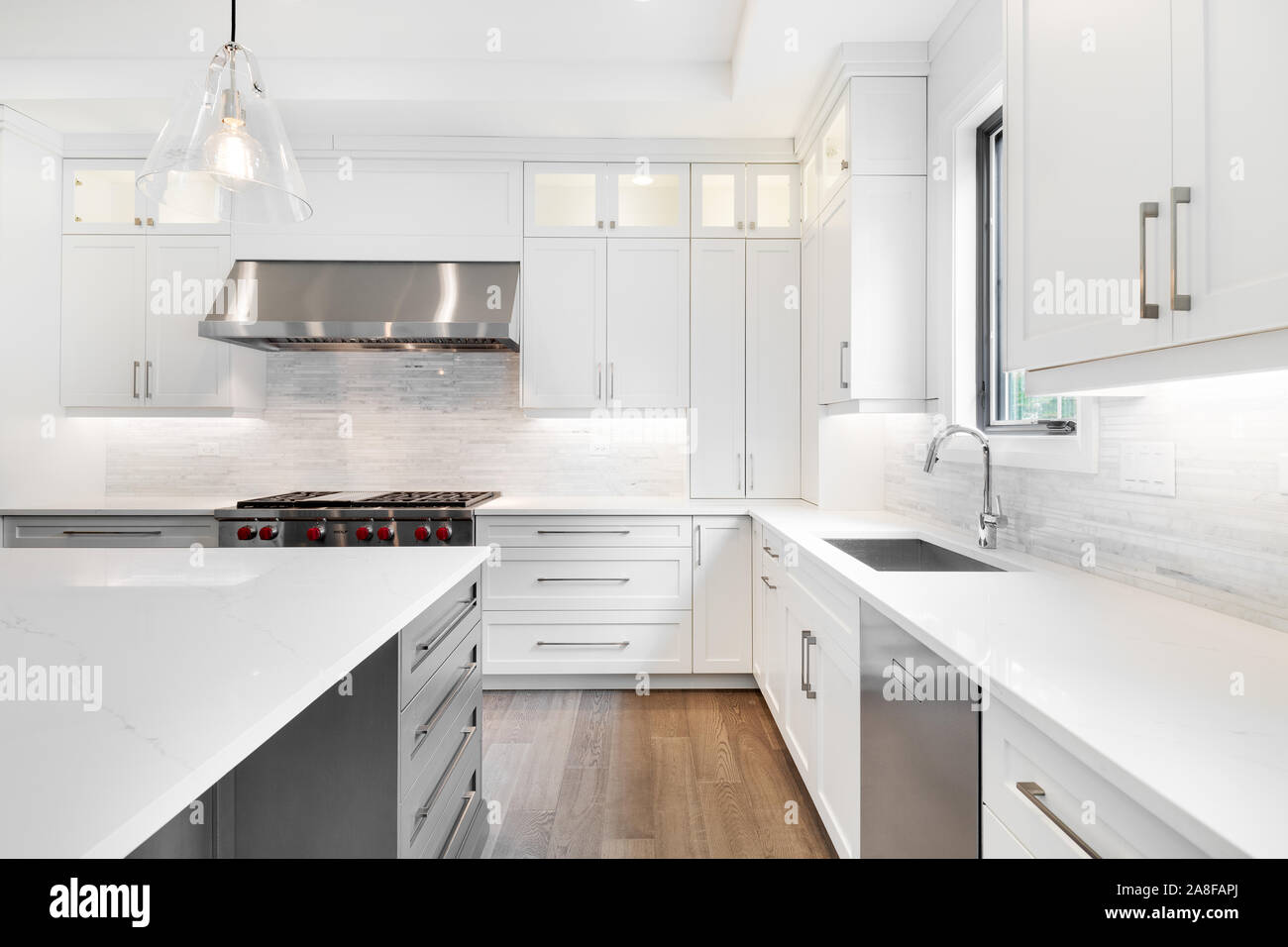 Una lussuosa cucina moderna con acciaio inossidabile Wolf elettrodomestici circondata da armadi bianchi, bello il granito e pavimenti in legno duro. Foto Stock