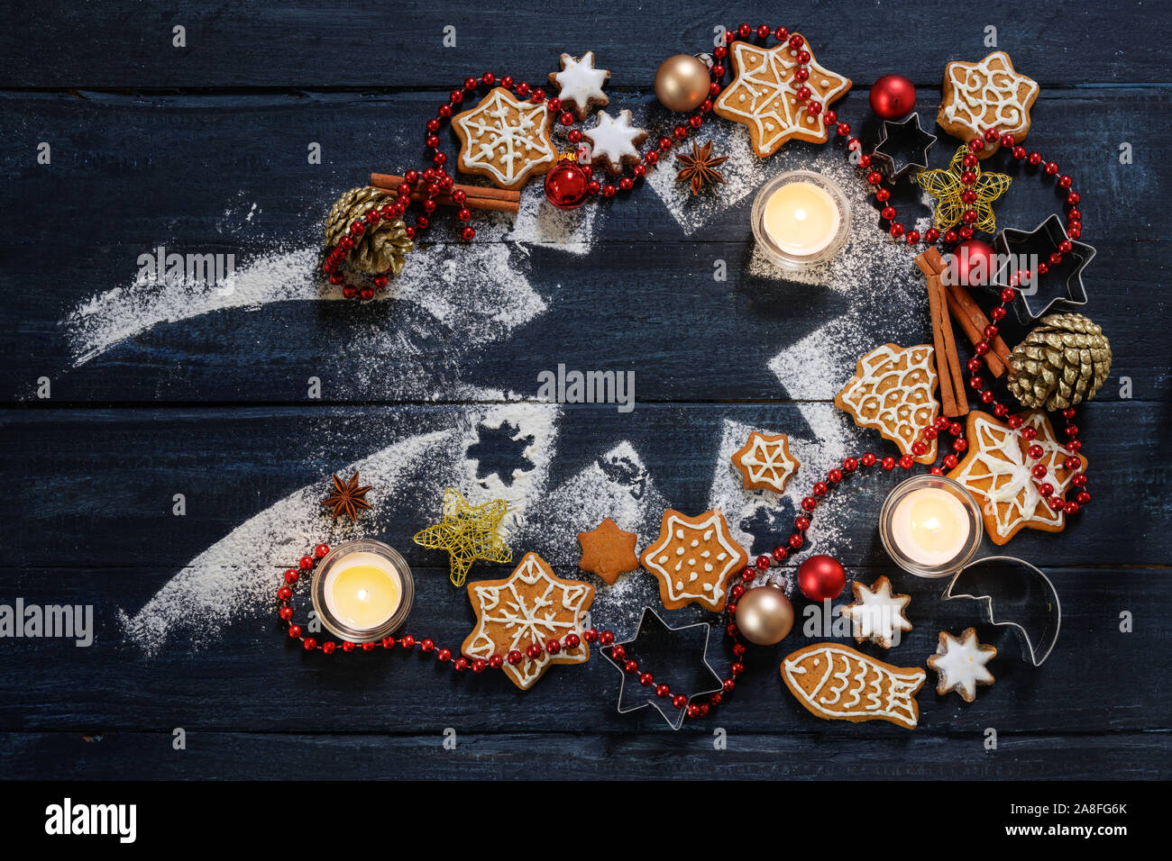 Gingerbread cookie, baubles di Natale, decorazione e candele accese su una stella cadente forma da zucchero a velo su un blu scuro legno rustico, laici piana w Foto Stock