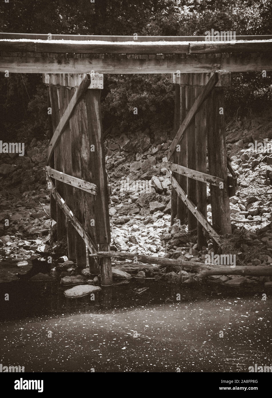 Ferrovia via attraverso una sgangherata traliccio in legno con acqua stagnante di seguito nel sud del Mississippi, Stati Uniti d'America, in granulosa seppia Foto Stock