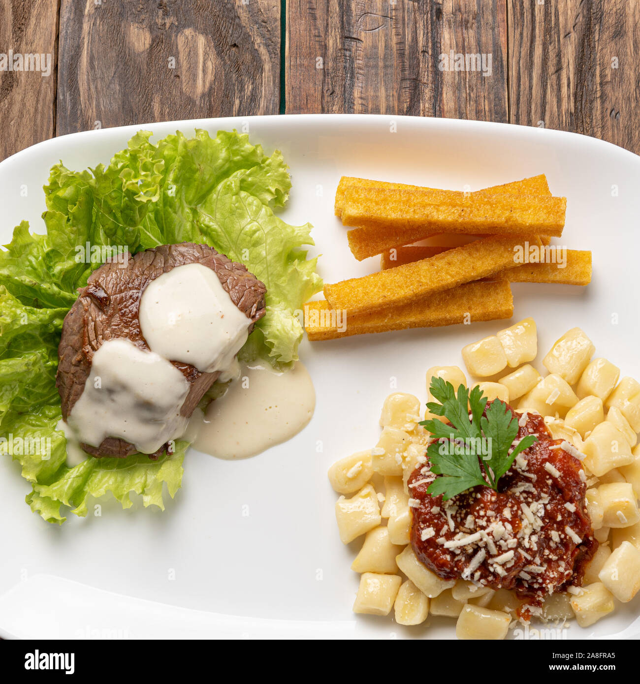 Gnocchi fatti in casa la pasta con la salsa di pomodoro e carne bovina mignon con salsa al formaggio in una piastra bianca su sfondo di legno Foto Stock