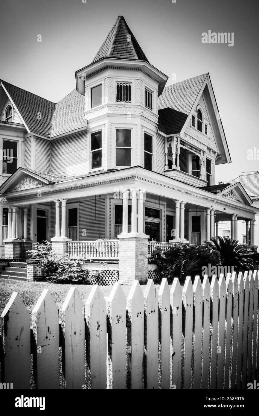 Un iconico white Picket Fence circonda un imponente stile Queen Anne Victorian House, costruita nel 1890, ora una ditta di legge, in Hattiesburg MS, USA, B & W Foto Stock