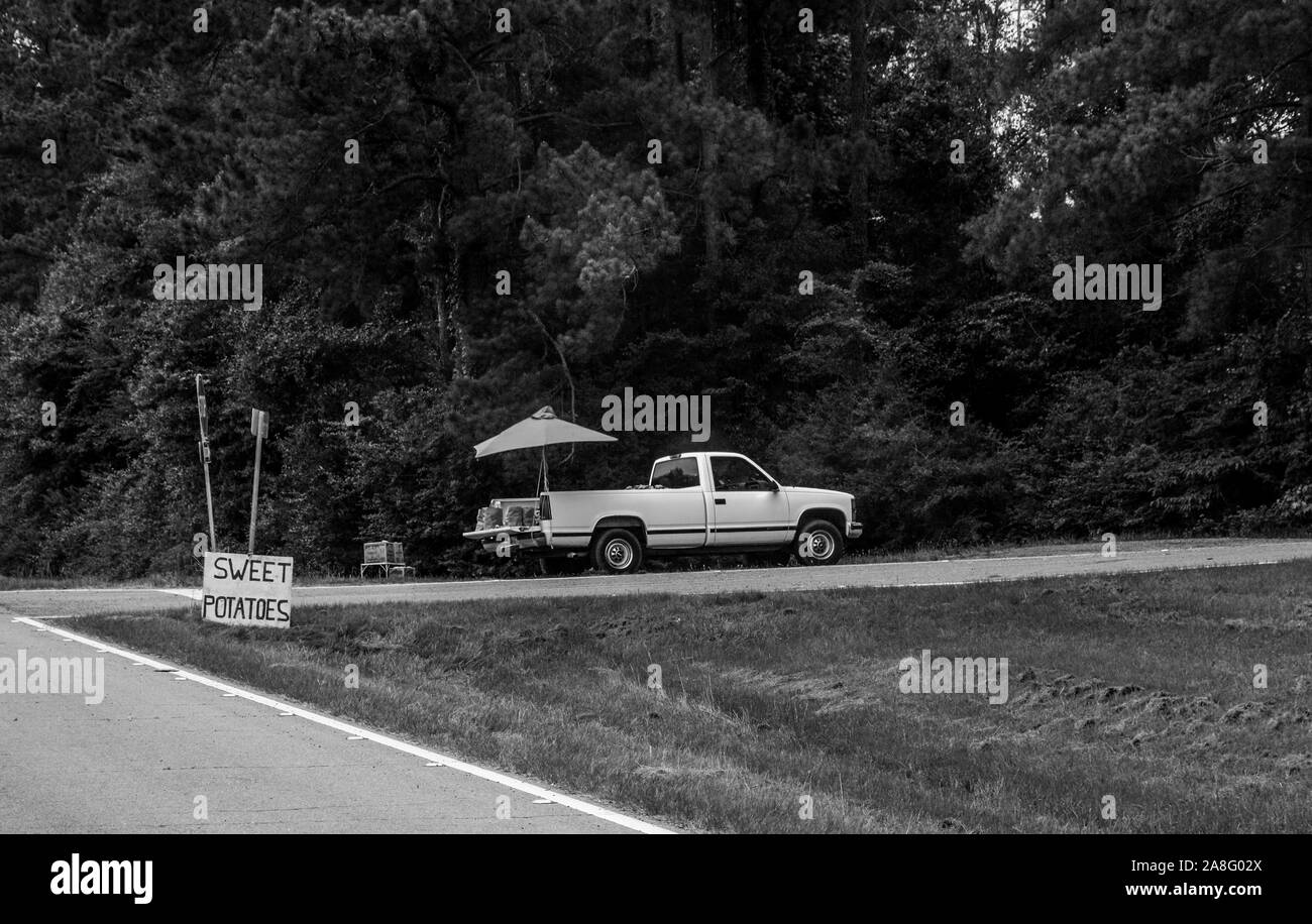 Un fornitore di produrre in un carrello di prelievo sul lato della strada con un segno di patate dolci nelle zone rurali del sud del Mississippi, Stati Uniti d'America, in bianco e nero Foto Stock