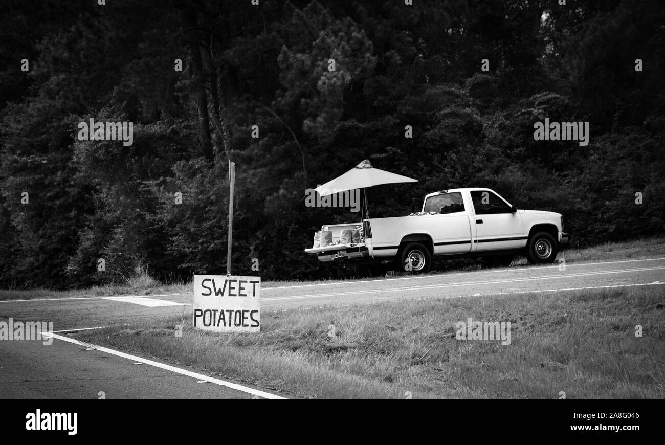 Un fornitore di produrre in un carrello di prelievo sul lato della strada con un segno di patate dolci nelle zone rurali del sud del Mississippi, Stati Uniti d'America, in bianco e nero Foto Stock