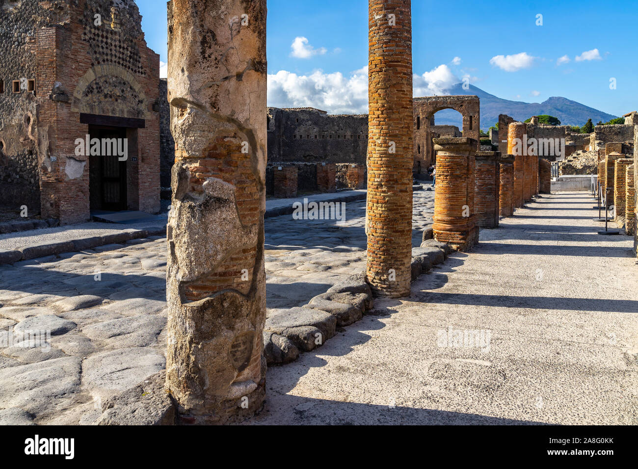 Resti di colonne romane di Pompei lungo Via del Foro con arco di Caligola e il Vesuvio sullo sfondo, Italia Foto Stock