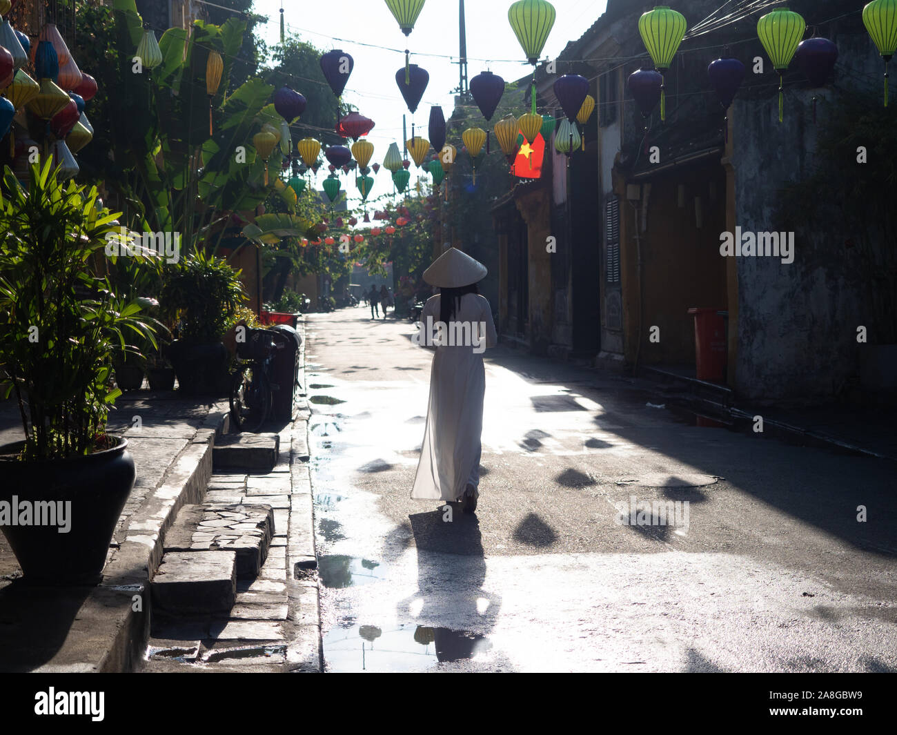 Il vietnamita donna che indossa un ao iam o tunica tradizionale e pantalone di tuta e non la o conica di cappello di paglia mentre si cammina al di sotto del tessuto lanterne in Hoi Un Foto Stock