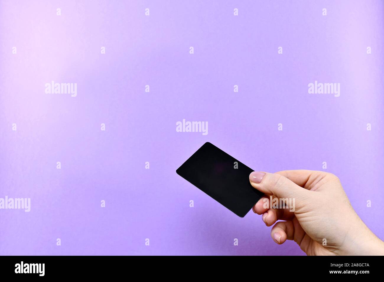 Dando un nero carta di credito o carta sconti con una mano su uno sfondo viola con lo spazio libero. Foto Stock