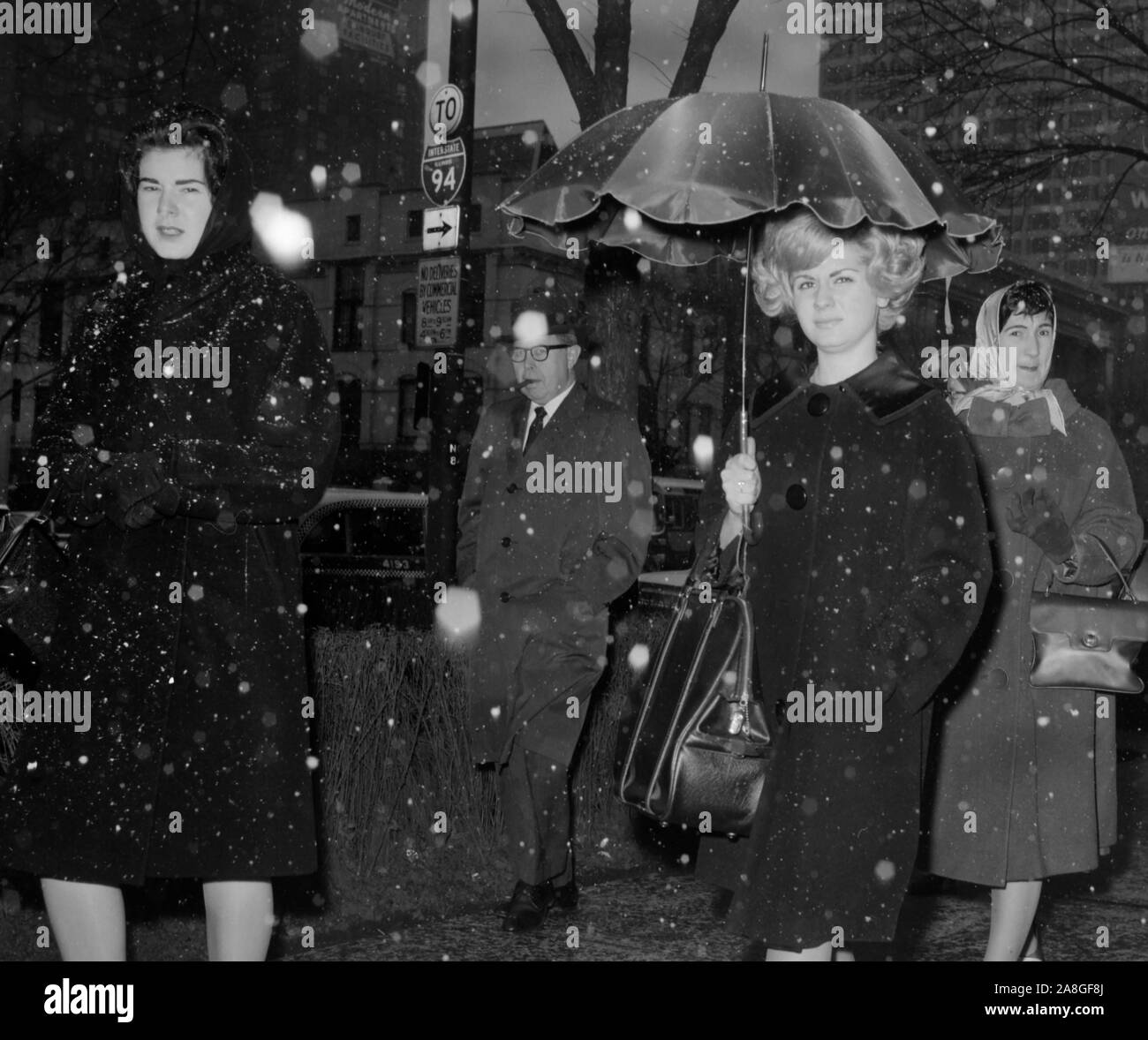 I pedoni a piedi lungo Michigan Avenue a Chicago come i fiocchi di neve cominciano a volare, ca. 1962. Foto Stock