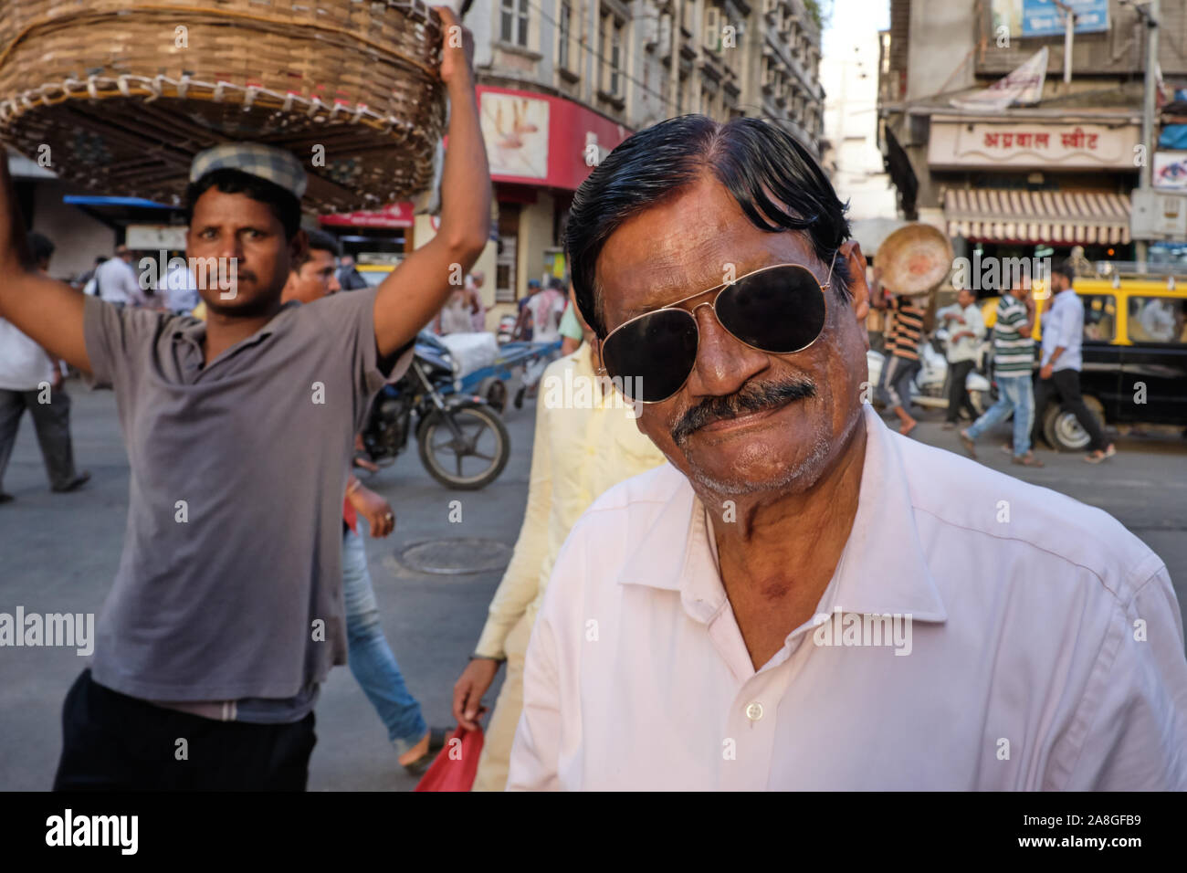 In Kalbadevi Road, Bhuleshwar, Mumbai, in India, in una zona commerciale, un commerciante tessile in posa per una fotografia, un portiere con il suo cesto passando da Foto Stock