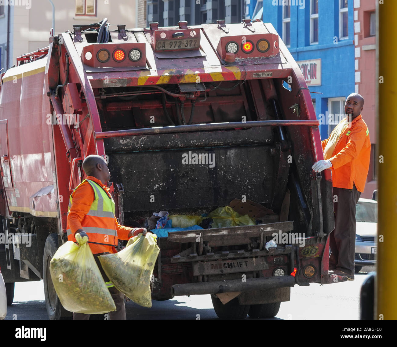 Camion della spazzatura e pattumiera uomini caricamento di sacchetti di rifiuti nel veicolo parcheggiato in una città urbana street a Cape Town, Sud Africa Foto Stock