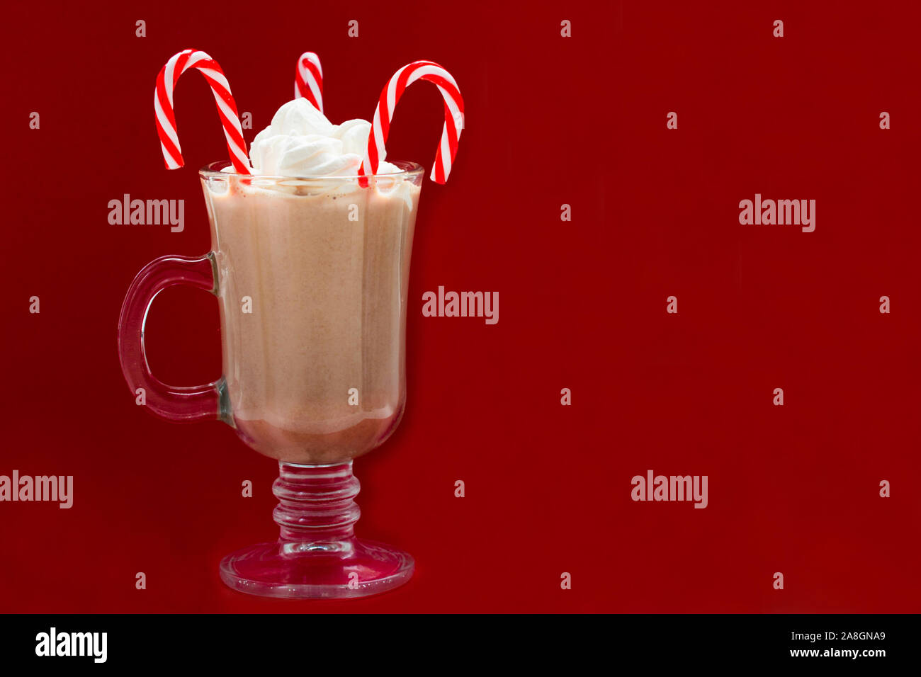Bicchiere di cioccolata calda con marshmallows e caramelle di Natale su uno sfondo rosso.Concetto bevande di Natale concetto. Copia dello spazio. Foto Stock
