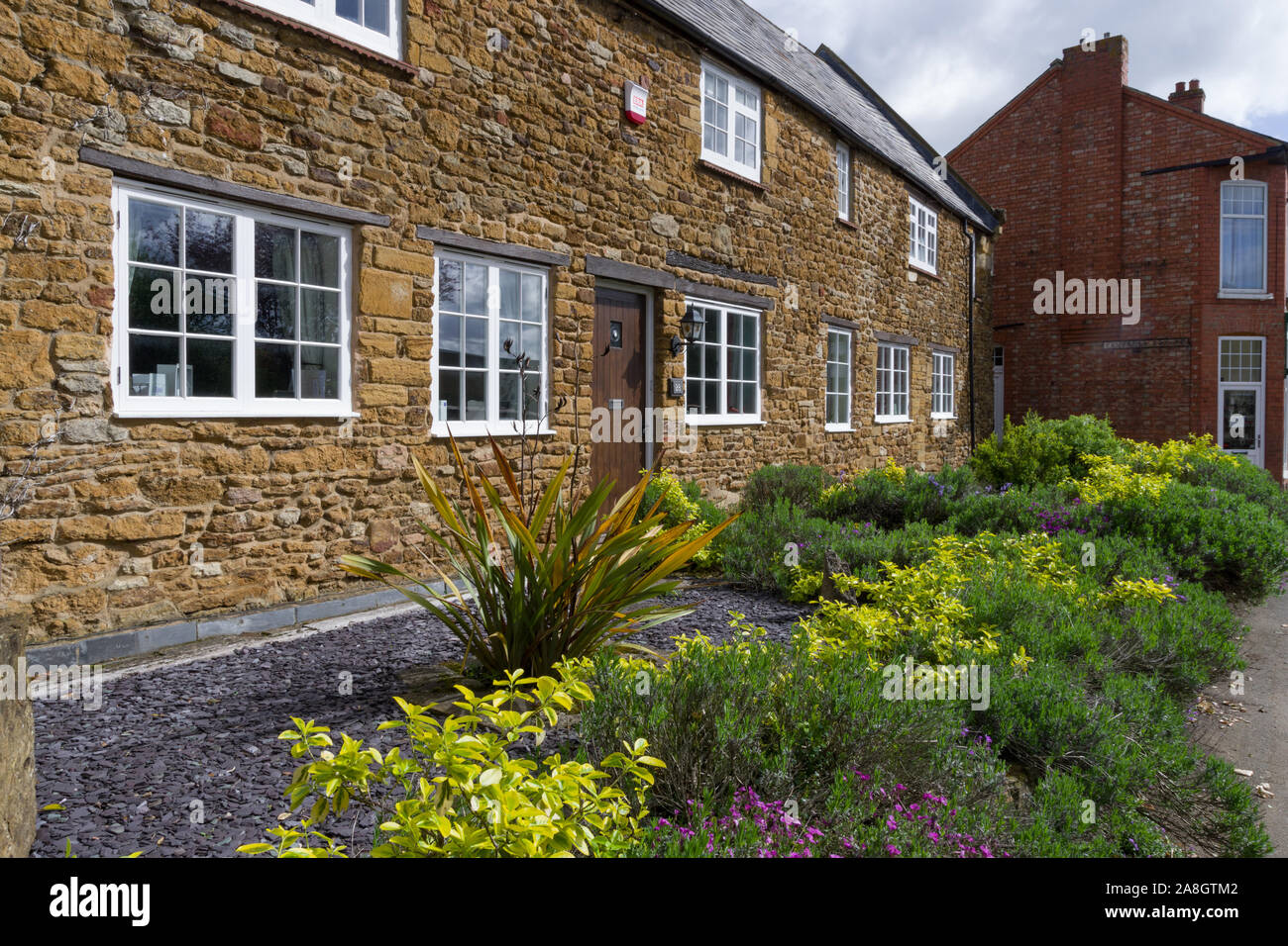 Terrazza della vecchia pietra costruito case con il piccolo ma coloratissimi giardini anteriore sulla High Street nel villaggio di Earls Barton, Northamptonshire, Regno Unito Foto Stock