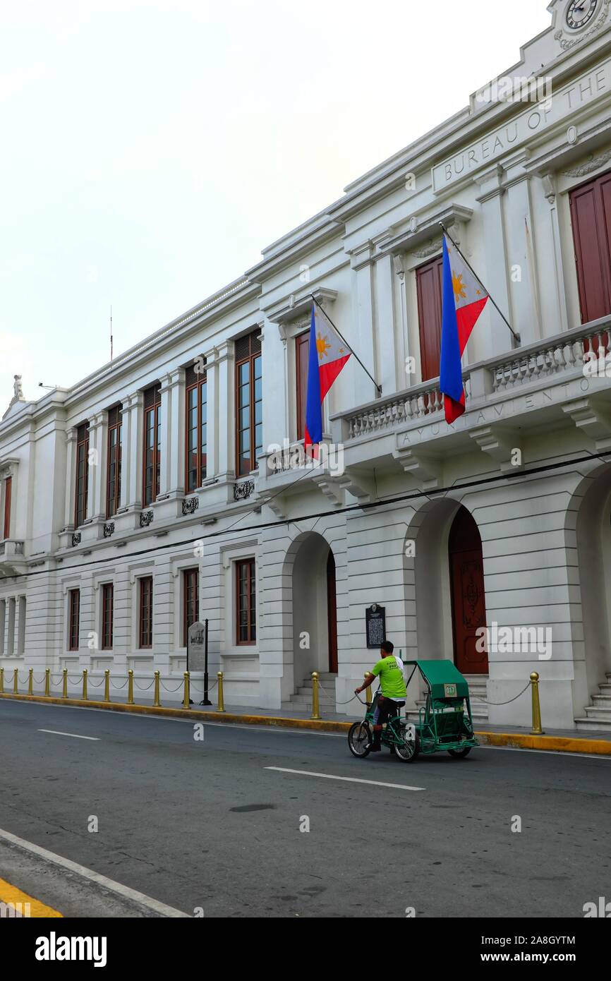 Un pedicab rigidi passato l' Ufficio di presidenza del Tesoro edificio di Intramuros, Manila, Filippine - 18 maggio 2019. Foto Stock