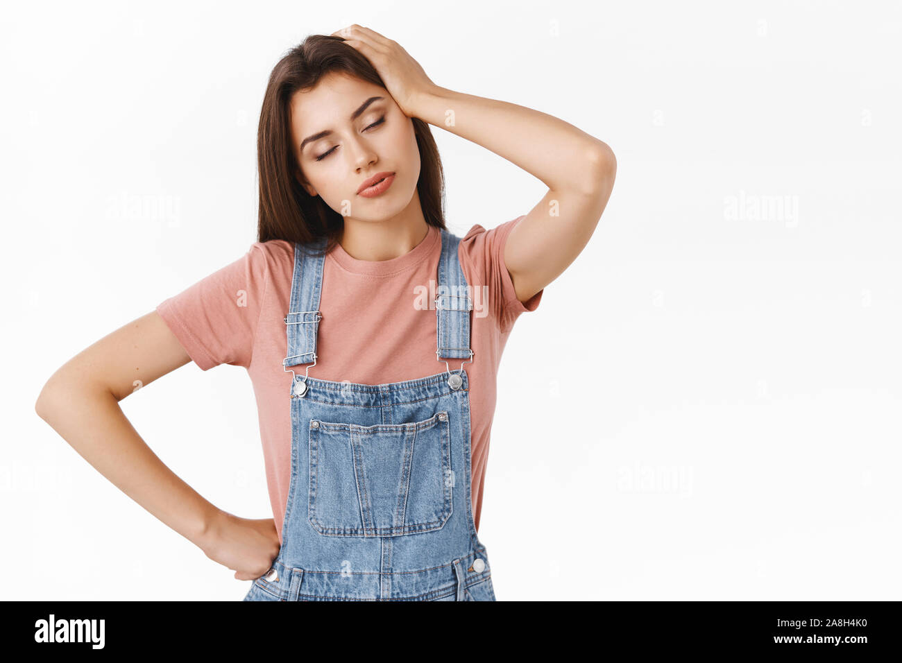 Ragazza sentirsi stanco dopo il turno di notte, testa inclinabile, toccando i capelli e chiudere gli occhi, sighint, tenere la mano sulla vita, in piedi turbato dalla fatica su bianco Foto Stock