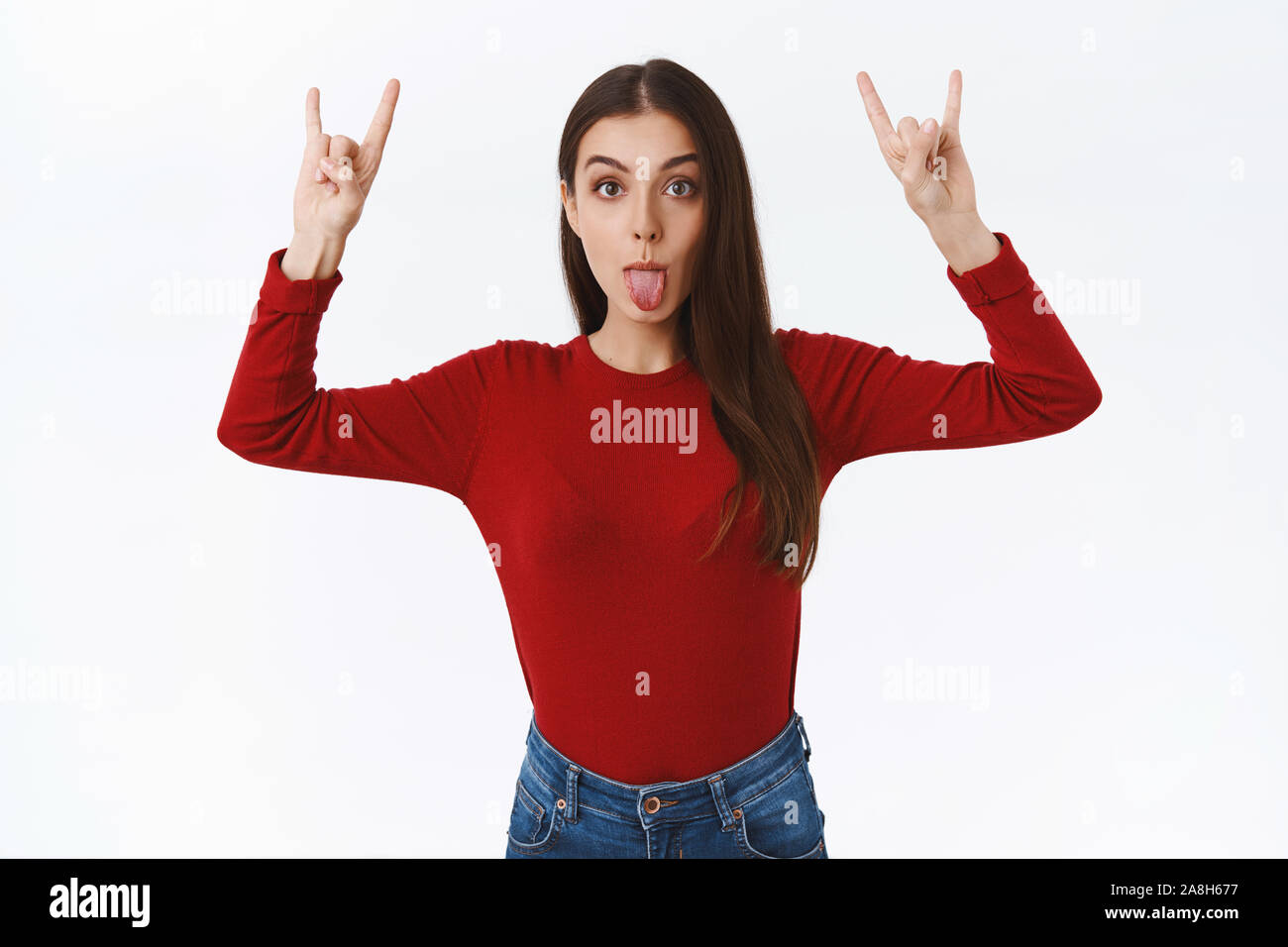 Giocoso e divertente e sciocco brunette girl in rosso maglione, alzando le mani in alto mostra il rock'n'roll, heavy metal segno, che mostra la linguetta con la goody expression Foto Stock