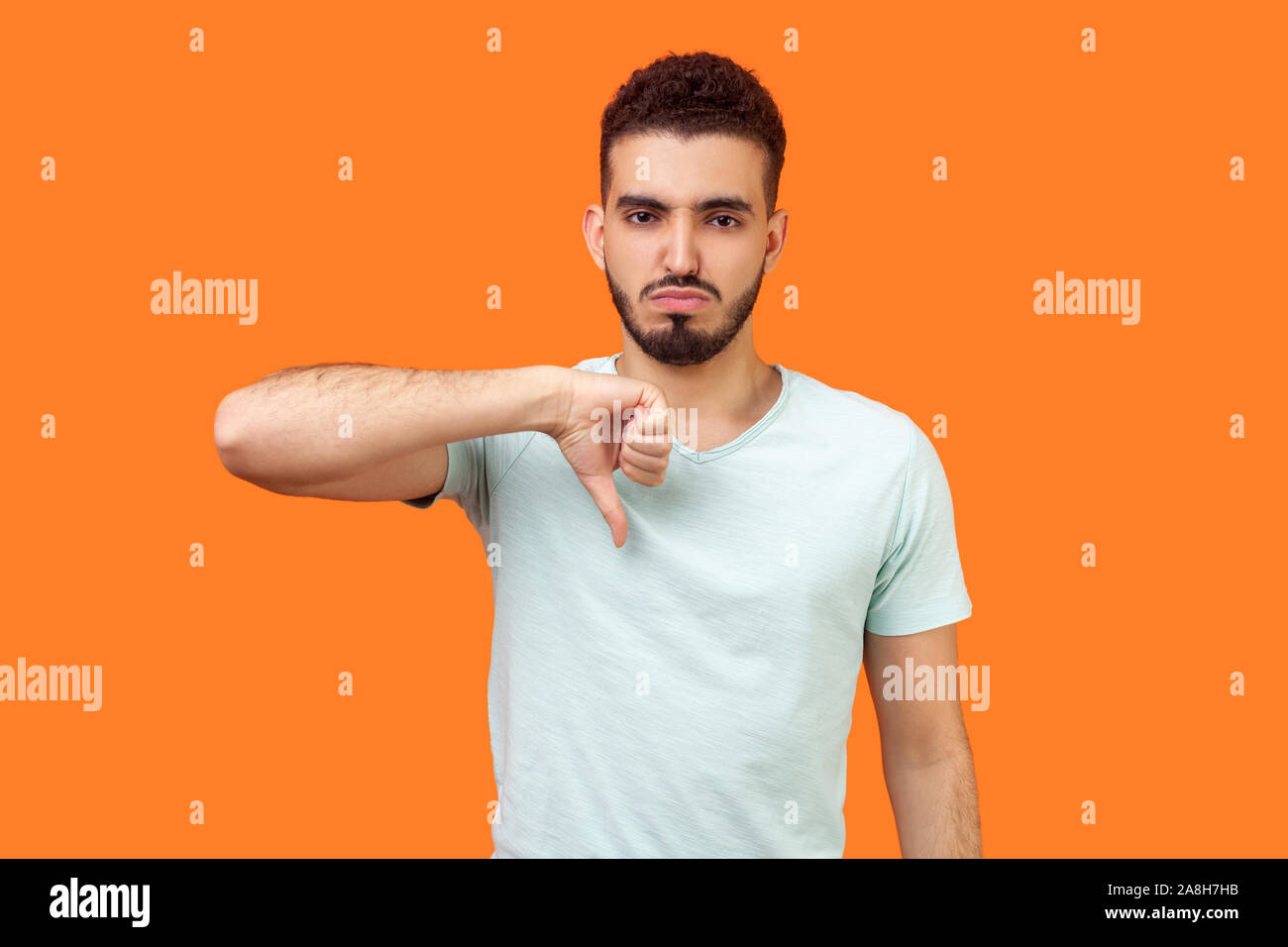 Pollice in giù! Ritratto di frustrato insoddisfatto brunette uomo con la barba in casuale t-shirt bianco mostra antipatia gesto, disapprovazione segno negativo. i Foto Stock