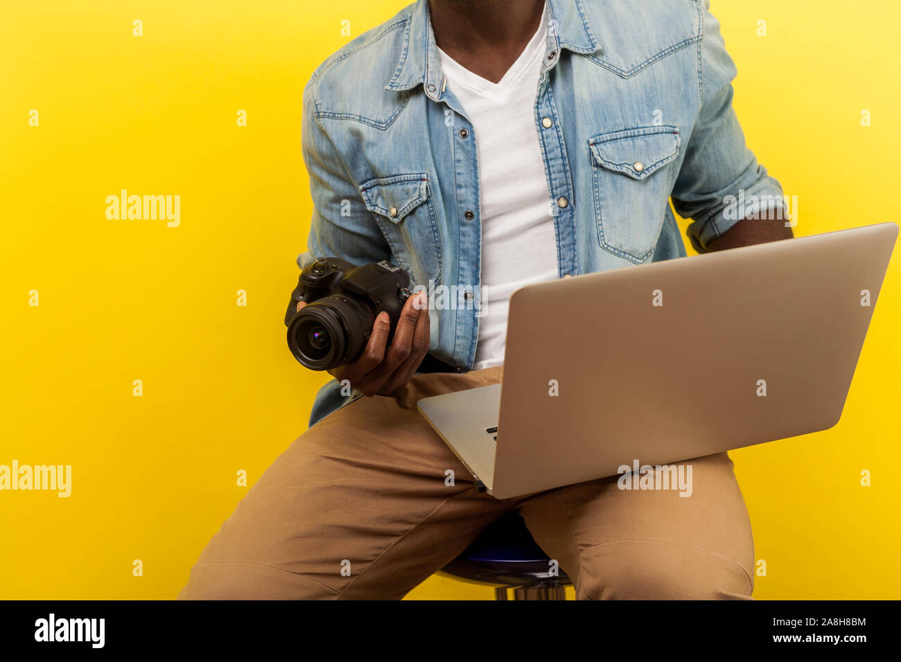 Ritagliato ritratto di fotografo maschio in denim shirt azienda digitale fotocamera DSLR e laptop, andando a prendere foto o creare un video utilizzando foto editin Foto Stock