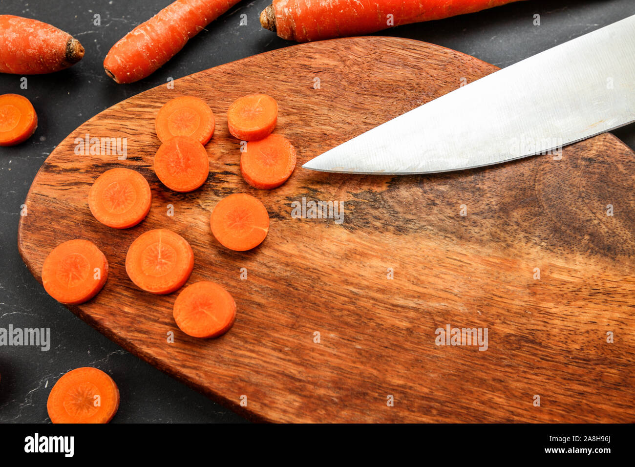Tagliere di legno (spazio per testo) con la carota tagliata per piccoli cerchi, la lama del coltello per cuoco visibile, vista dall'alto. Foto Stock