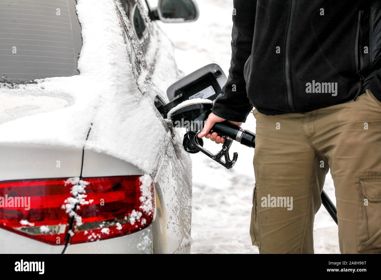L'uomo il suo riempimento coperto di neve auto diesel il serbatoio di gas in corrispondenza della pompa del carburante, dettaglio sulla mano e ugello di benzina. Foto Stock