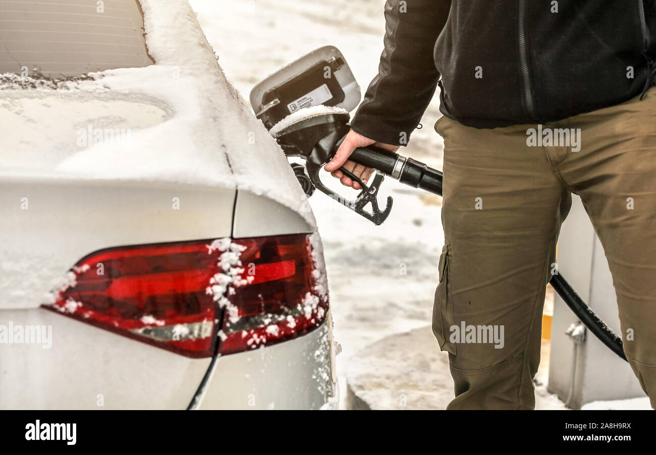 Riempimento di uomo coperto di neve auto diesel il serbatoio di gas in corrispondenza della pompa del carburante, dettaglio sulla mano e ugello di benzina. Foto Stock