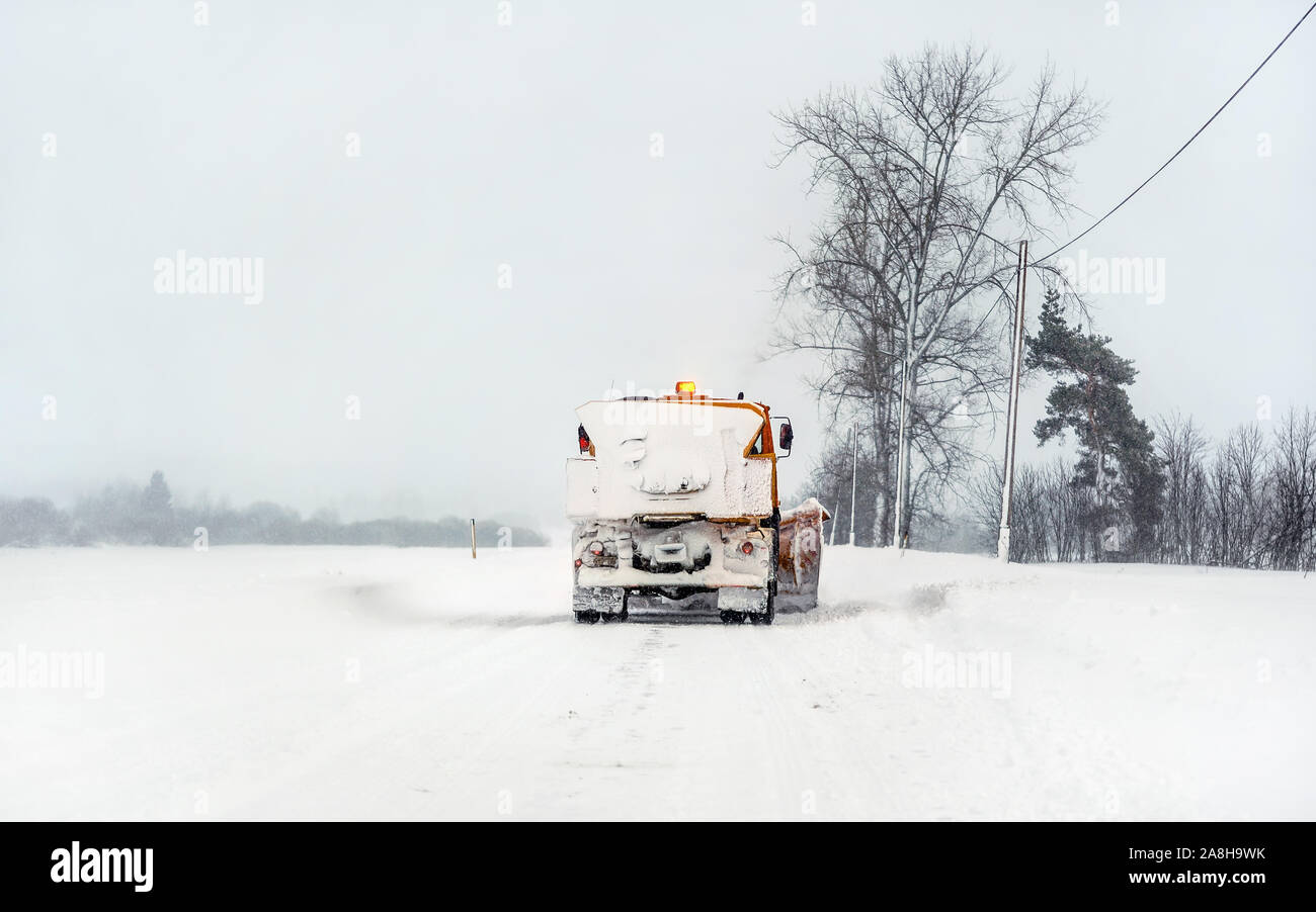 Aratro arancio carrello su strade coperte di neve road, cielo grigio e gli alberi in background - Manutenzione Invernale Strade Foto Stock