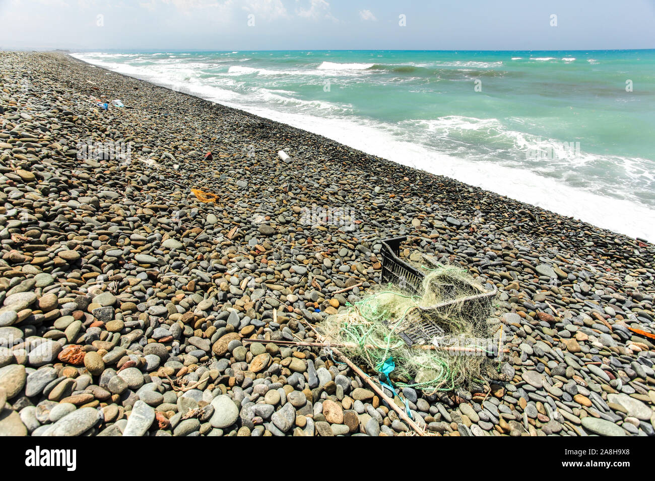 Bella wild ruvida piccole pietre ghiaiosa spiaggia, rovinato con spazzatura - rimane nero della scatola di plastica e le reti da pesca. Ambiente oceano littering conc Foto Stock