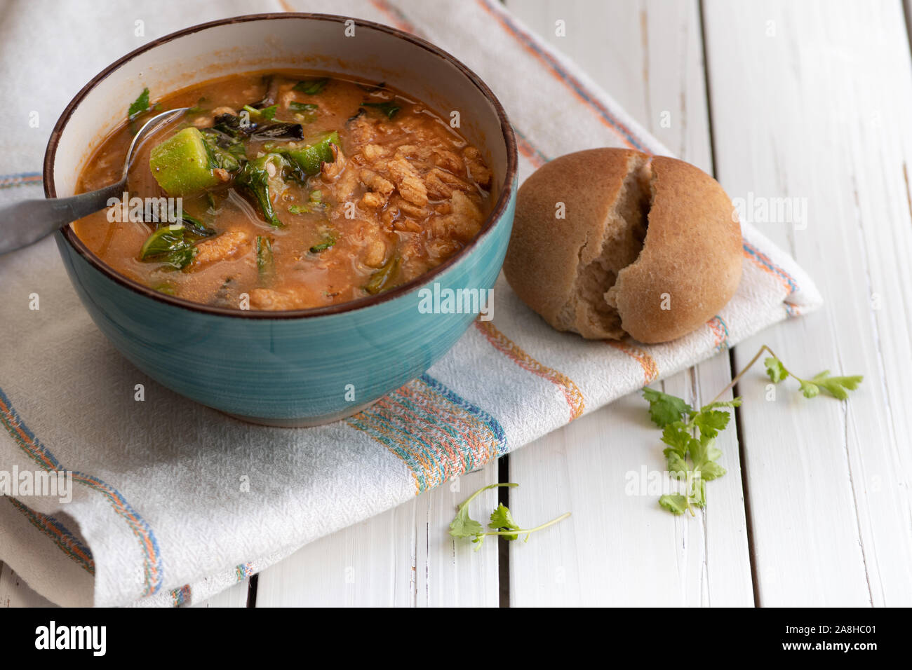 Vegano sostanziosa zuppa di riso marrone, okra e spinaci, servita in una ciotola su una bianca tavolo in legno Foto Stock