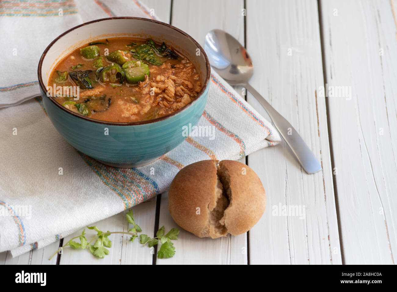 Vegano sostanziosa zuppa di riso marrone, okra e spinaci, servita in una ciotola su una bianca tavolo in legno Foto Stock