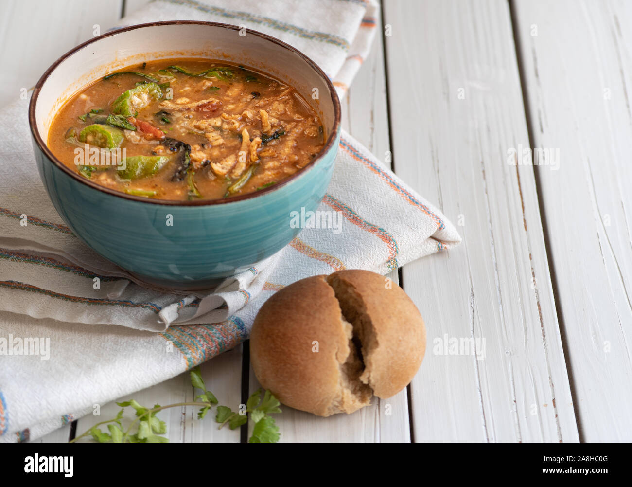 Vegano sostanziosa zuppa di riso marrone, okra e spinaci, servita in una ciotola su una bianca tavolo in legno Foto Stock