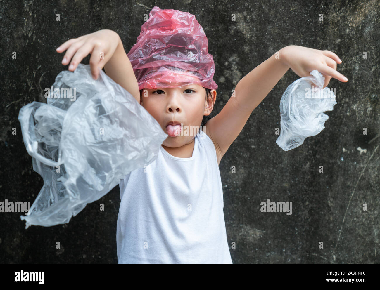 Carina ragazza del bambino è in possesso di sacchetti di plastica. La plastica è sul suo capo. Concetto di smettere di usare il sacchetto in plastica. Foto Stock
