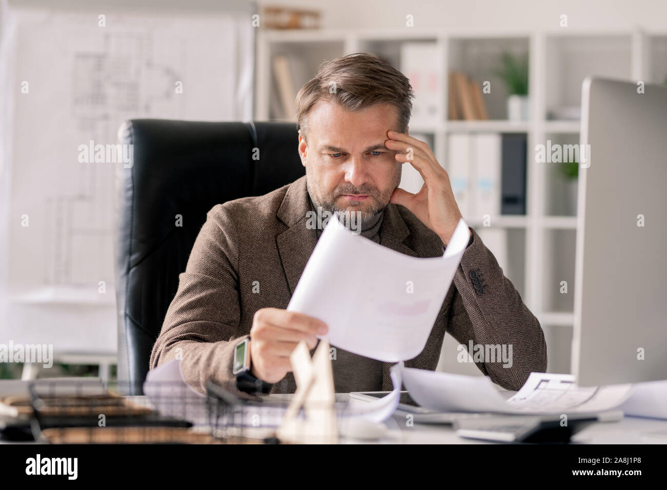 Malinconici architetto guardando il disegno sulla carta mentre si concentrano sul lavoro Foto Stock