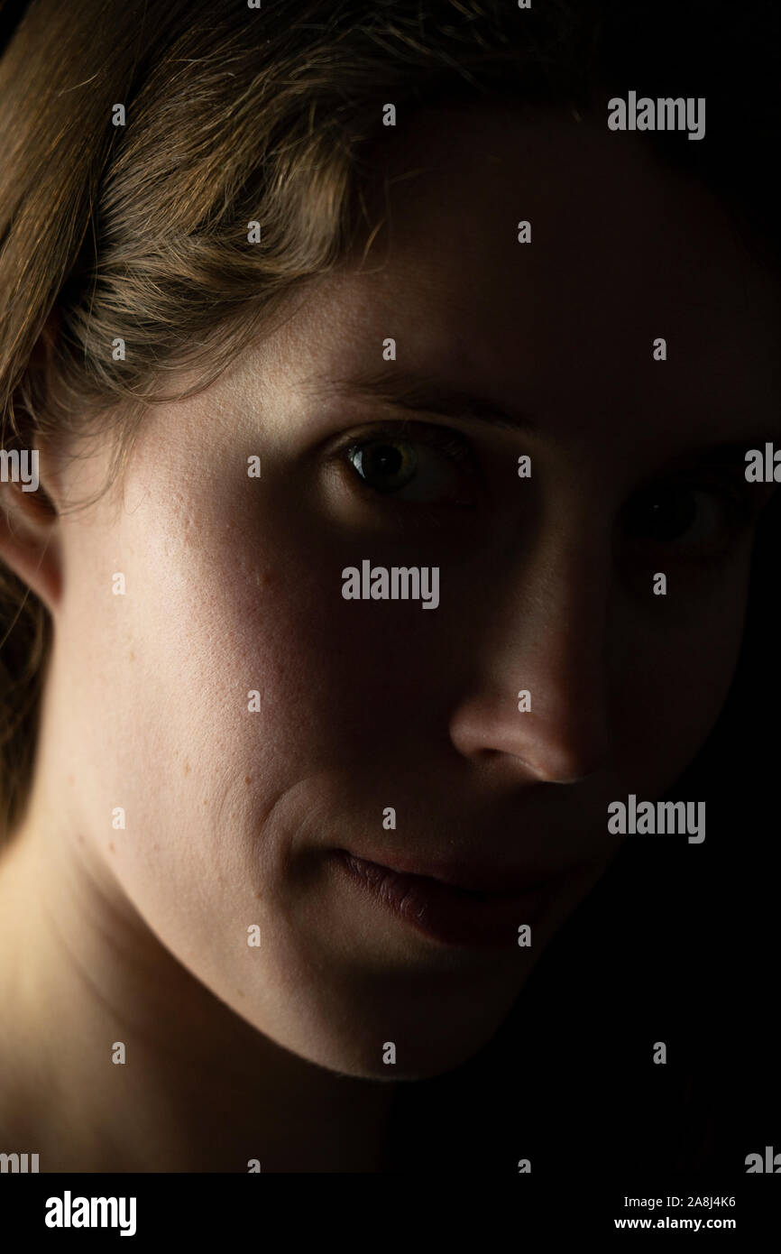 Un primo piano del profilo laterale di una giovane volto di donna che guarda direttamente lo spettatore con un mezzo sorriso e una misteriosa espressione Foto Stock