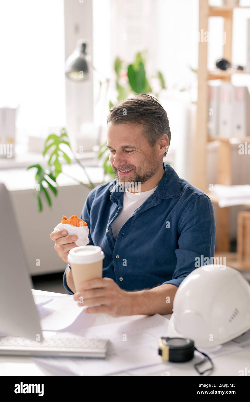 Felice ingegnere matura guardando funny cupcake in mano prima di mangiarla Foto Stock